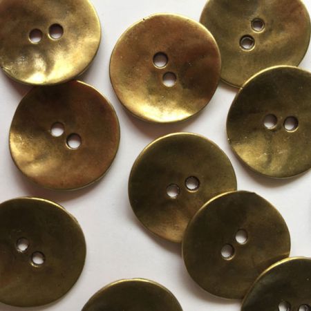 Brass metal button with uneven surface.